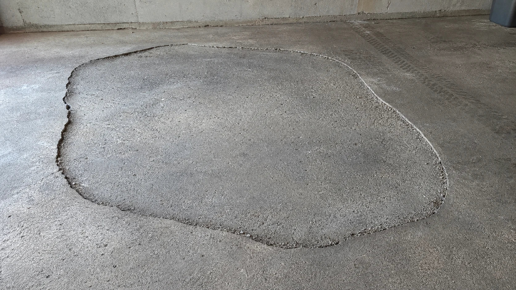 Dalle de garage affaissée avec une fissure qui suit le contour de la zone tassée, avant réparation