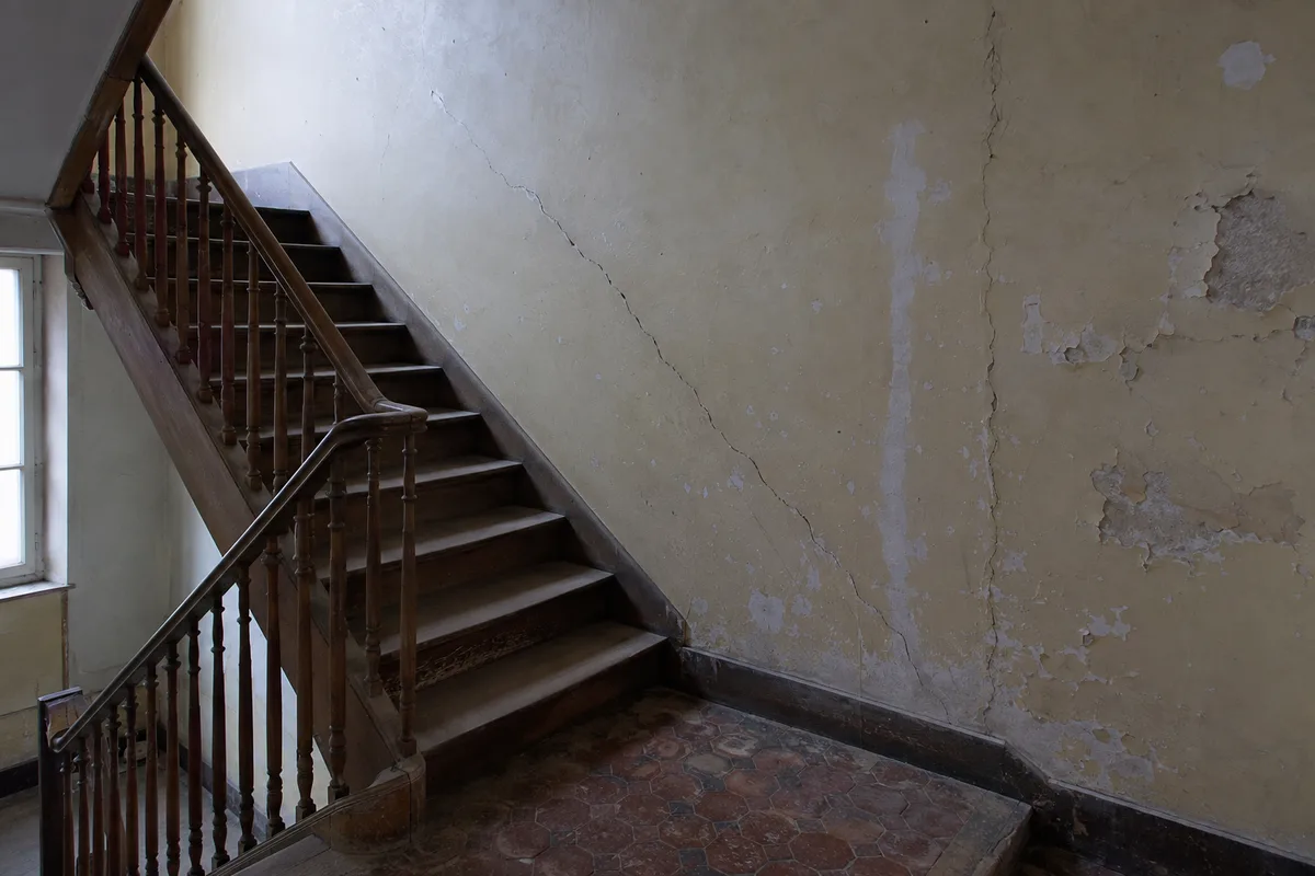 Cage d'escalier d'un immeuble d'habitation ancien avec fissures sur le mur porteur et l'enduit dégradé, aucune personne dans le cadre