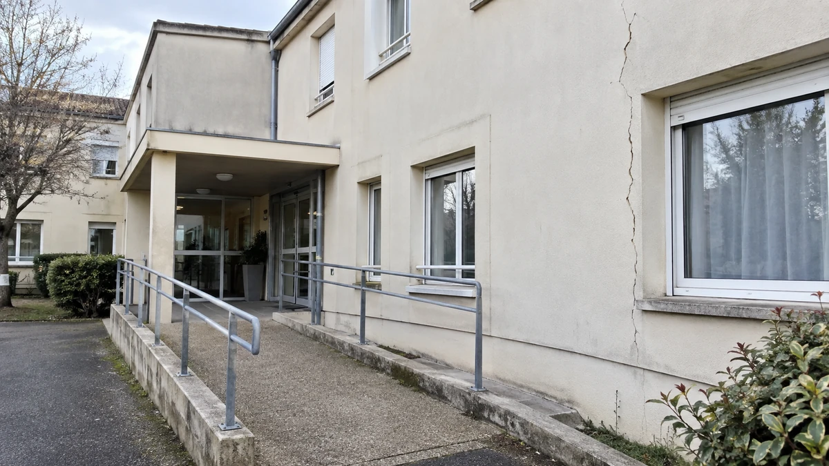 Façade d'un bâtiment d'EHPAD francilien avec une fissure verticale nette près d'une fenêtre de chambre, rampe d'accès visible, aucune personne dans le cadre