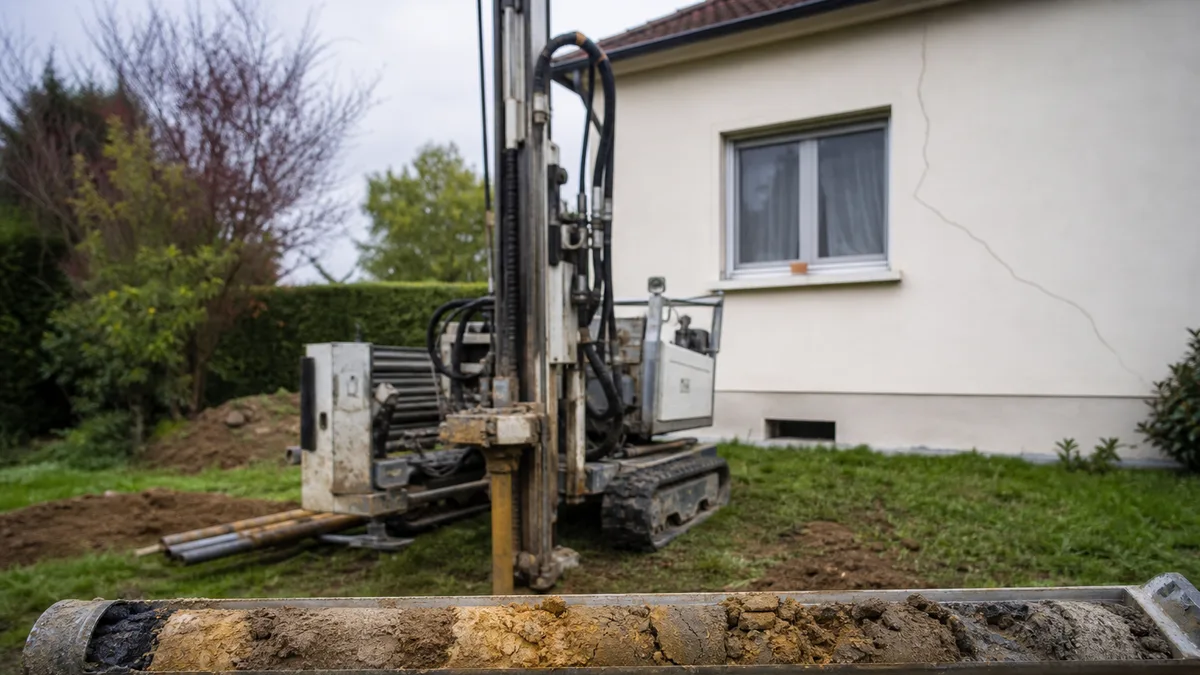 Foreuse de sondage géotechnique installée dans le jardin d'un pavillon francilien, carotte de sol extraite posée à proximité, aucune personne dans le cadre