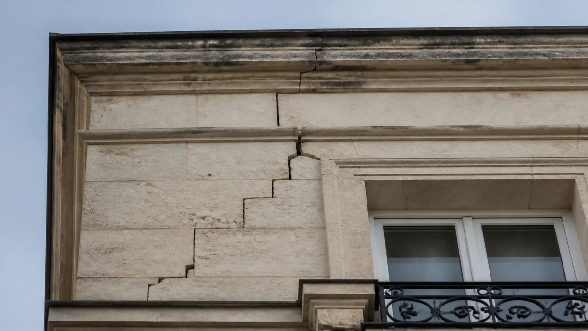 Façade en pierre de taille d'un immeuble haussmannien parisien avec une fissure en escalier qui suit les joints des pierres au-dessus d'une fenêtre à garde-corps en fonte