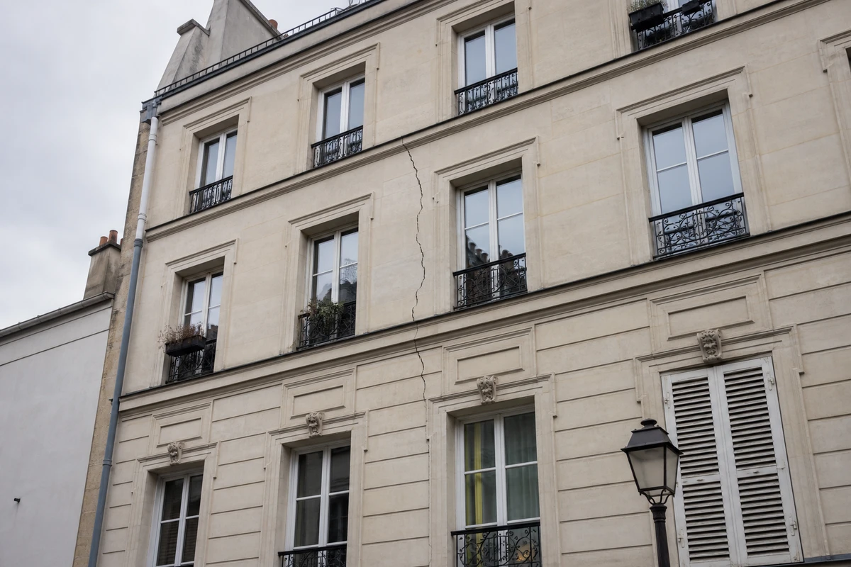 Façade d'un immeuble haussmannien francilien avec une fissure visible entre deux fenêtres, cage d'escalier commune en arrière-plan