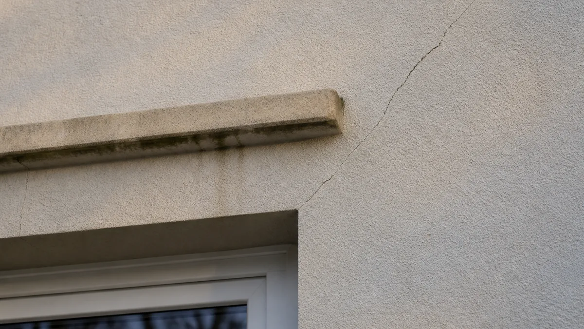 Fissure fine parcourant l'enduit d'une façade de maison récente au droit d'un angle de baie, aucune personne dans le cadre