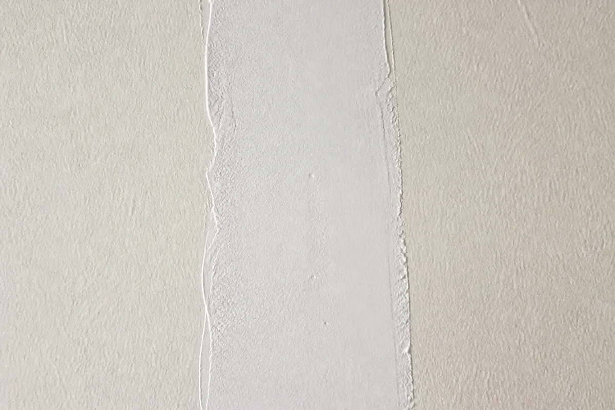 Gros plan d'une fissure de mur fraîchement rebouchée avec une bande d'enduit blanc lissé, prête à être poncée et repeinte