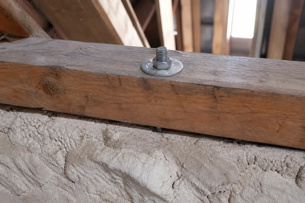 Jonction entre une sablière en bois et un mur de maçonnerie dans un comble, fixation d'ancrage métallique visible avec un léger décalage