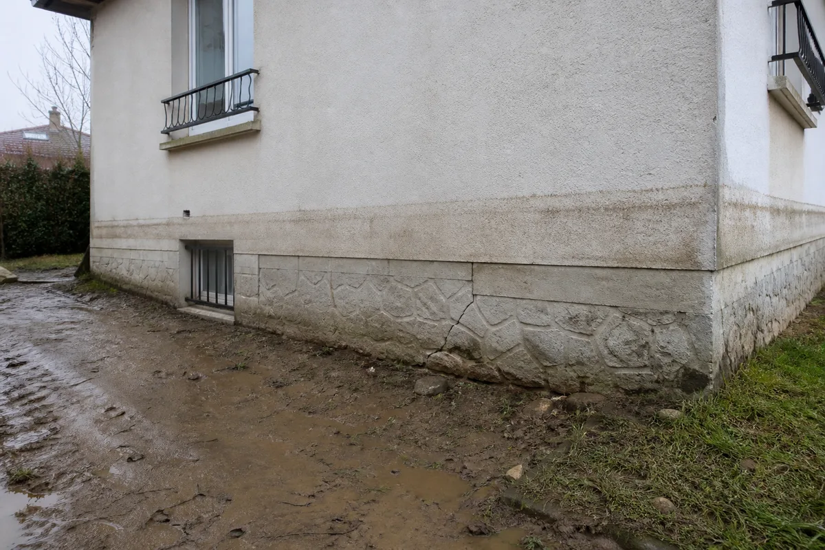 Façade d'un pavillon francilien avec une trace de ligne d'eau de crue encore visible sur le soubassement et une fissure verticale à proximité, aucune personne dans le cadre