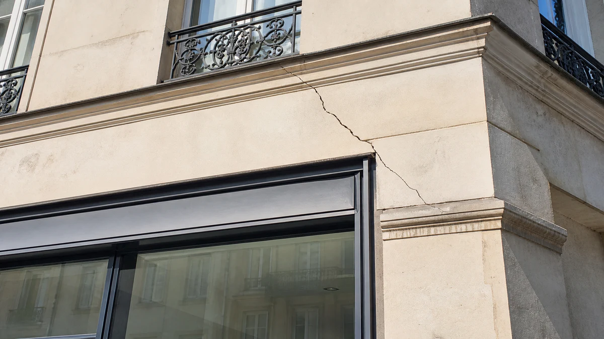Vitrine d'un local commercial en rez-de-chaussée avec une fissure nette visible sur le pilier de façade entre deux vitrages, aucune personne dans le cadre