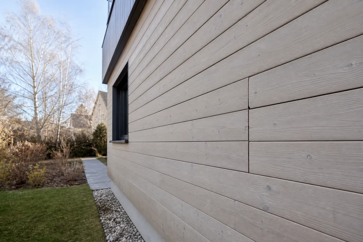 Façade d'une maison à ossature bois avec bardage clair, chantier récent, léger désordre visible à la jonction de deux panneaux, aucune personne dans le cadre