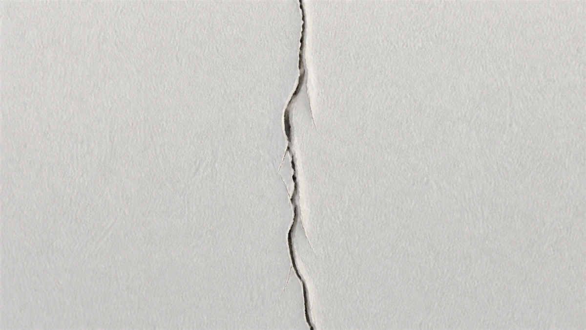 Gros plan sur une façade fraîchement repeinte où une fissure a rouvert la nouvelle couche de peinture en suivant exactement le tracé de l'ancienne fissure sous-jacente