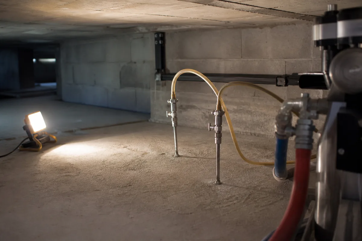 Lances d'injection de résine expansive plantées à travers une dalle béton dans un vide sanitaire, tuyaux de pompage reliés, aucune personne dans le cadre