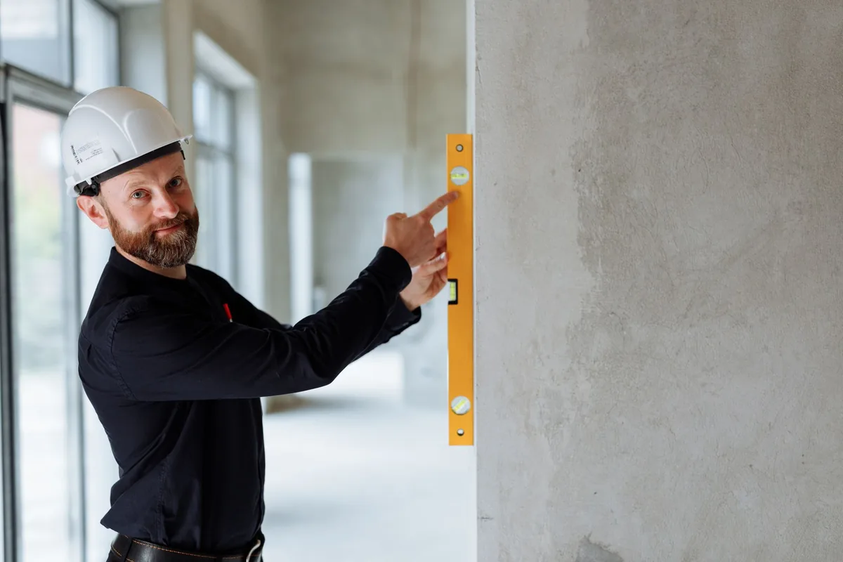 Expert utilisant un niveau pour réaliser un diagnostic visuel de fissure sur un mur