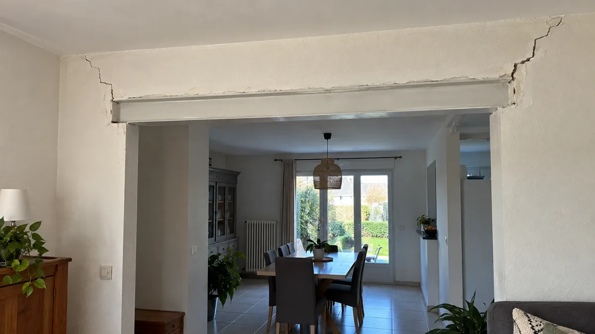 Ouverture pratiquée dans un mur porteur intérieur avec linteau métallique apparent, fissures en escalier partant des deux angles supérieurs de la baie dans l'enduit, aucune personne dans le cadre