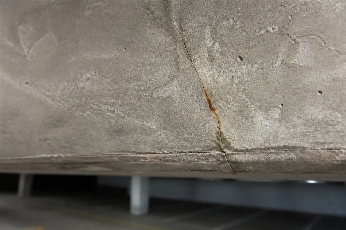 Poutre en béton armé fissurée en sous-face avec une légère trace de rouille au droit de la fissure, dans un parking souterrain ou sous-sol