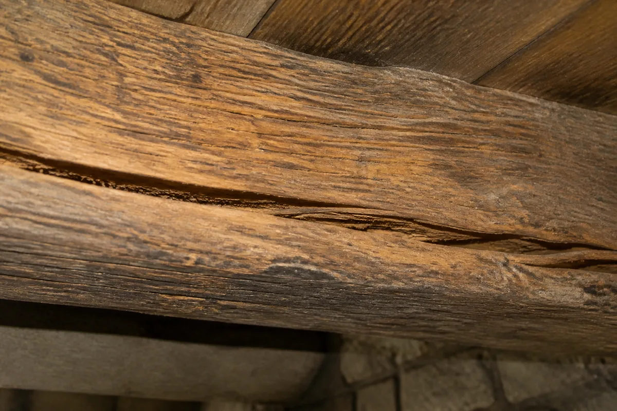 Gros plan sur une poutre en bois fissurée en sous-face, avec une fente longitudinale et une légère flèche visible, en sous-sol ou garage francilien