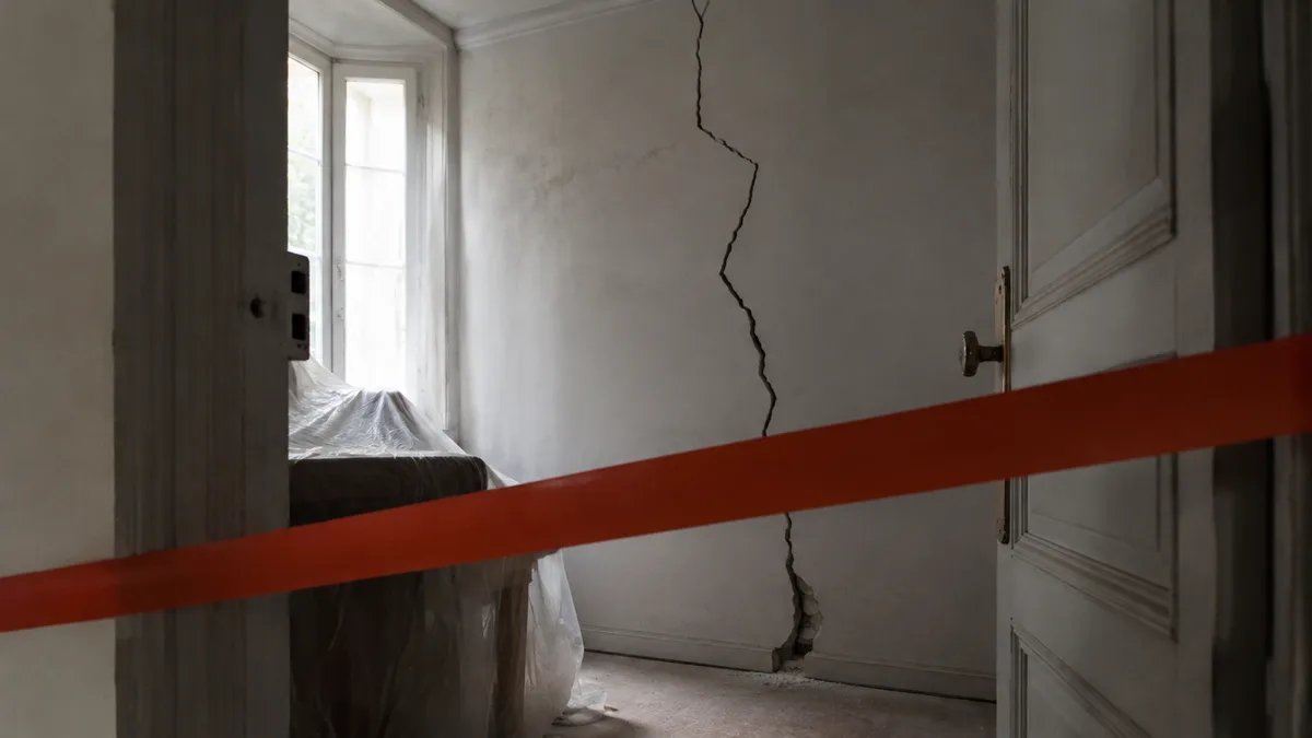 Pièce d'habitation vidée et condamnée, mobilier bâché, fissure traversant le mur porteur, aucune personne dans le cadre