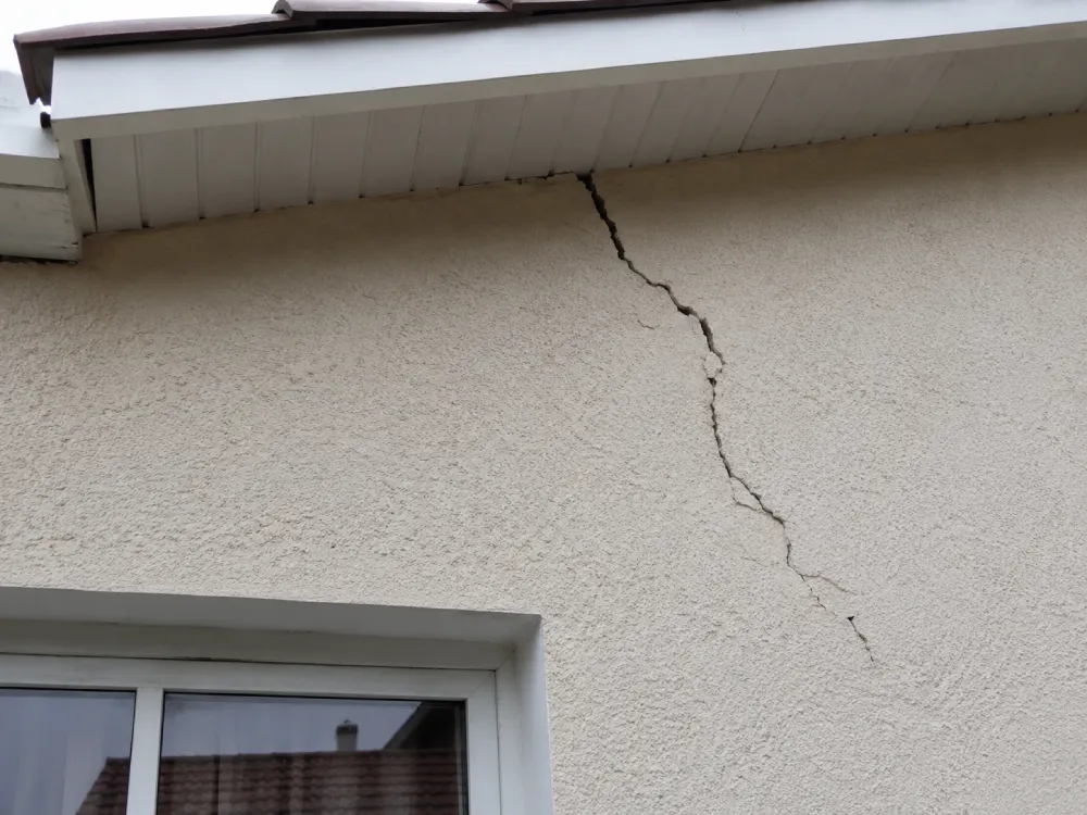 Fissure fine en façade, partant d'un angle de toiture, illustrant la diversité des formes de fissures possibles sur un bâti.