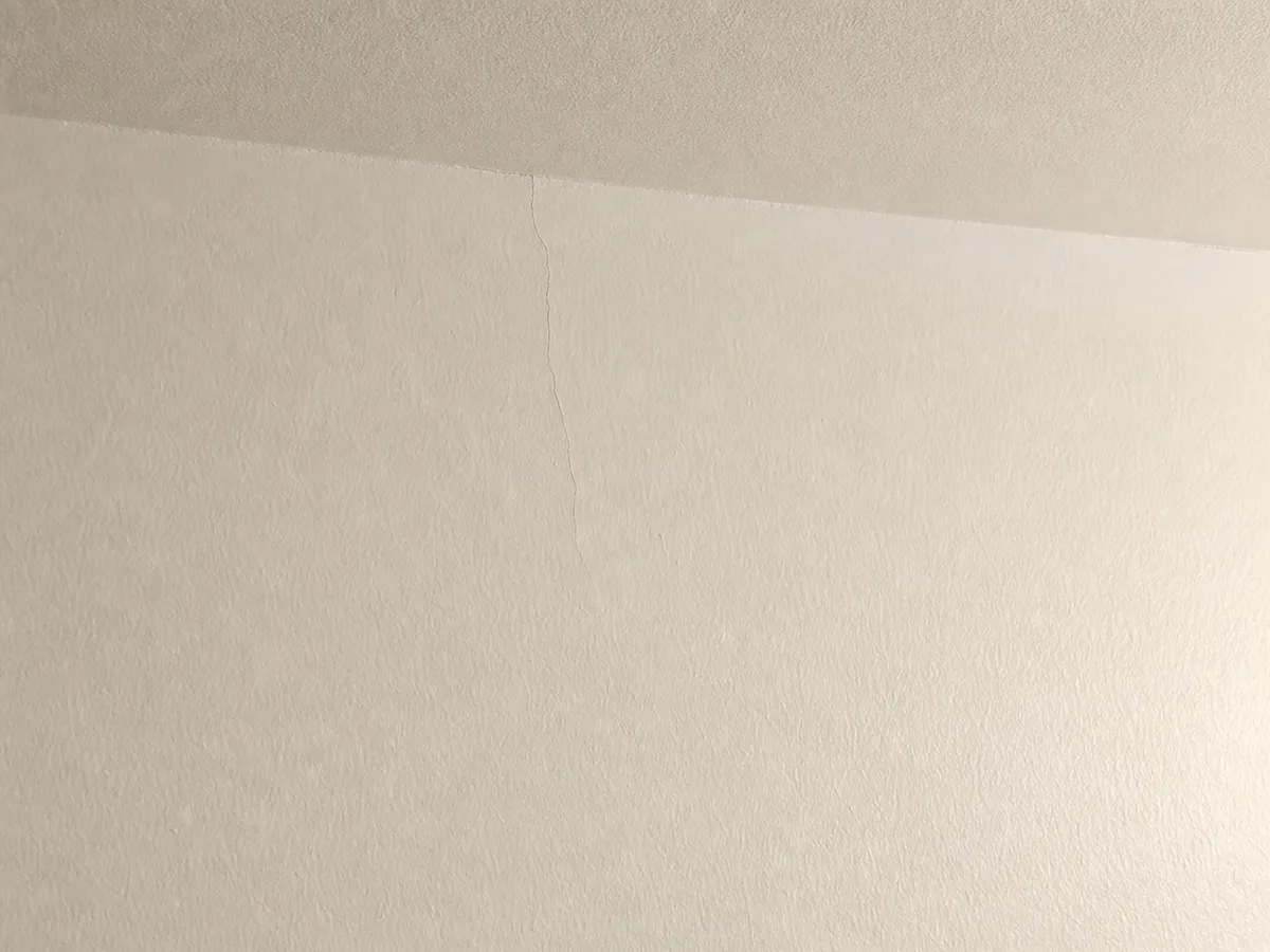 Microfissure capillaire non traitée sur un mur intérieur en plâtre, avant intervention